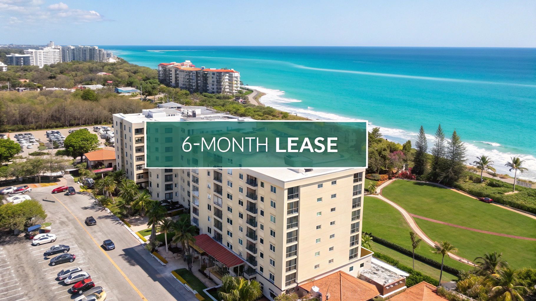 Aerial view of beachfront apartment buildings next to turquoise ocean water, with a banner overlay reading "6-MONTH LEASE." Lush greenery and a parking lot are visible beside the buildings.