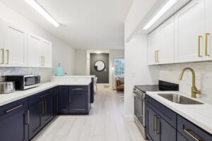 Modern kitchen with white upper cabinets, navy blue lower cabinets, gold handles, stainless steel appliances, and a marble countertop—an inviting feature often found in upscale Boca Raton apartments near FAU.