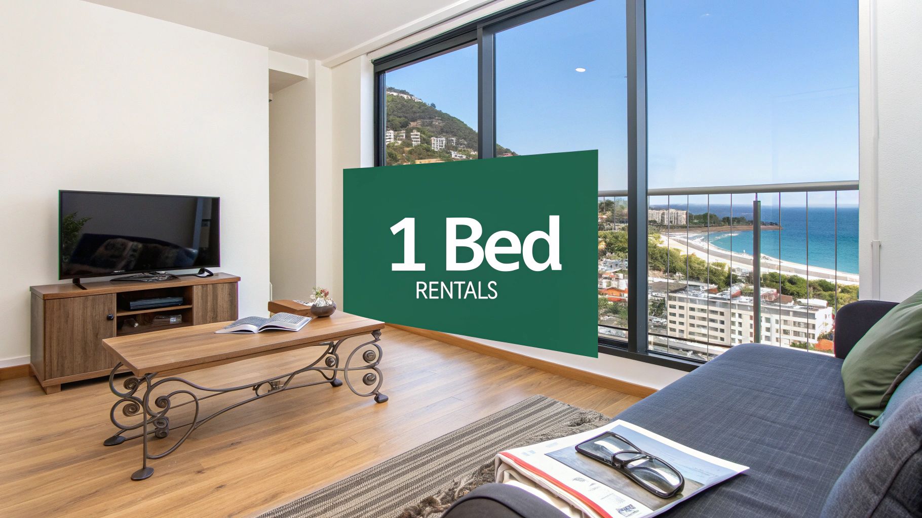 A modern living room with a wooden floor, TV, coffee table, and couch, featuring large windows overlooking the beach and ocean. A green sign reads "1 Bed Rentals.